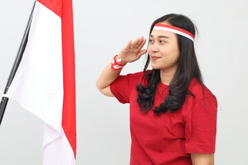 Indonesian woman standing while saluting the Indonesian red and white flag, isolated on white...