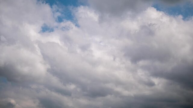 Ominous timelapse of dark grey storm clouds gathering and moving quickly across an overcast sky, showing dense cloud layers completely covering the blue, creating a threatening pre-storm mood.