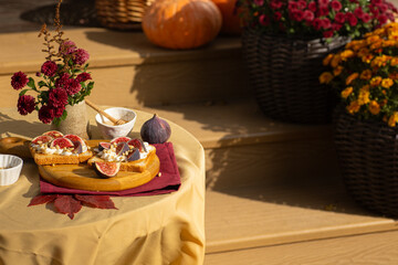 Cozy autumn table decoration for a thanksgiving party outdoors. Italian Bruschetta with creme cheese, figs, pine nuts and honey on a wooden board.