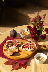 Cozy autumn table decoration for a thanksgiving party outdoors. Italian Bruschetta with creme cheese, figs, pine nuts and honey on a wooden board.