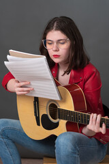 Female guitarist studying, analyzing sheet music for acoustic guitar. Her focus on precise musical execution and understanding is evident, as she diligently studies sheet music to prepare performance