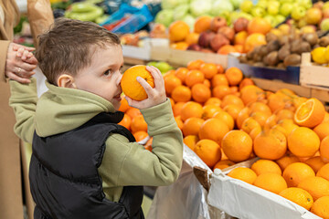 Little boy and his mom buy tangerines, oranges and green apples at farmer's market. Healthy nutrition concept. High quality photo