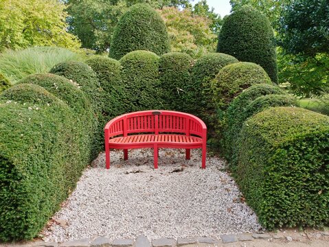 Rote halbrunde Parkbank vor Hecke