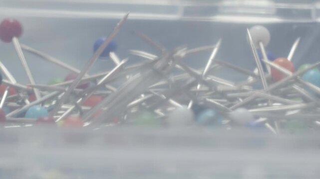 Close up of colored sewing pins with metallic heads inside a transparent plastic container, macro shot.