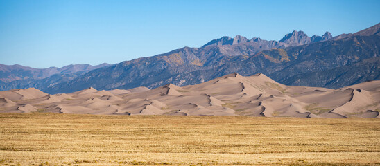 Panoramic view of Great Sand Dunes National Park in Colorado, USA. Desert landscape and golden meadow in autumn against the clear blue sky. The tallest dunes in North America.