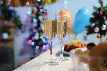 Two glasses of champagne on a festive table with blurred Christmas decorations and warm holiday lights in the background, symbolizing celebration and joy.