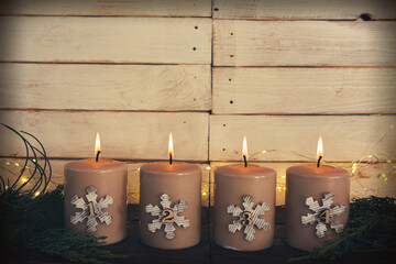 Four lit advent candles. Burning candles for the fourth advent. Simple christmas decoration with four candles in front of a light wooden plank wall with space for text.