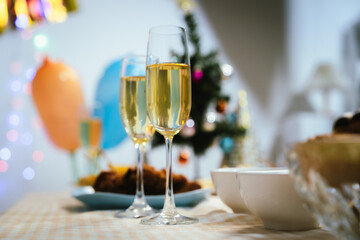 Two glasses of champagne on a festive table with blurred Christmas decorations and warm holiday lights in the background, symbolizing celebration and joy.