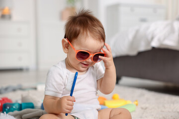 Cute baby with sunglasses and hair brush at home