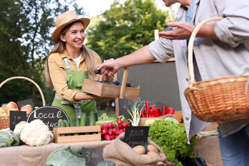 Man choosing fresh vegetables and plums from stall at farmer's market, closeup