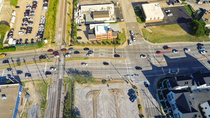 Railroad tracks and Cooper Street corridor in Arlington, Texas during peak traffic, flat-roof retail buildings, new development townhomes, mixed-use district with strong commuter and student flow