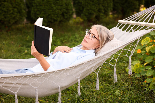 Senior woman reading book in hammock outdoors