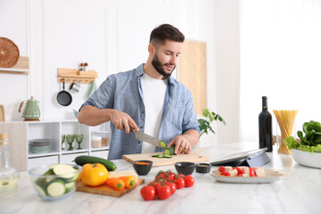 Smiling man looking at recipe on tablet while cooking at table in kitchen