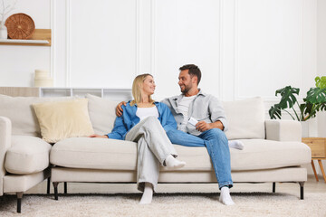 Couple with air conditioner remote control on sofa at home