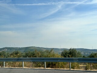 Fototapeta premium Scenic rural landscape with wind turbines on a hill under a clear blue sky. Renewable energy concept highlighting clean power, sustainability, and harmony between technology and nature.
