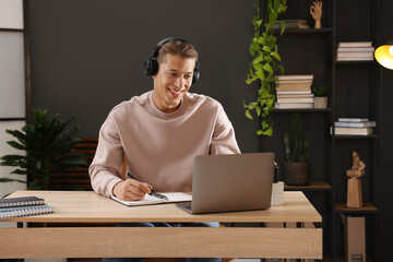 Man in headphones passing online test via laptop at table indoors