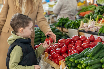 Side view unrecognizable mom and little boy son buying fresh cucumbers and tomatoes at farmer's market. Healthy nutrition concept. High quality photo