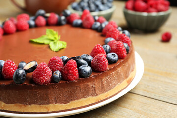 Delicious chocolate cheesecake with berries and mint on wooden table, closeup
