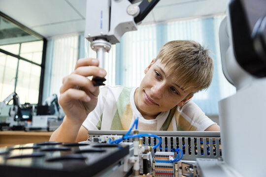 Smiling student testing robotic arm gripper in school tech lab. Concept of STEM education, robotics learning, hands on engineering, automation systems, and youth innovation in technology.