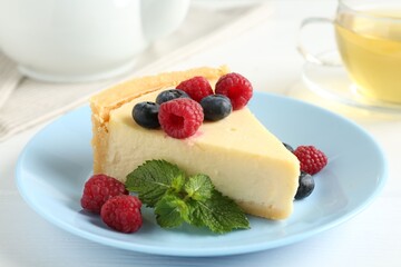 Piece of delicious cheesecake with fresh berries and mint on white table, closeup
