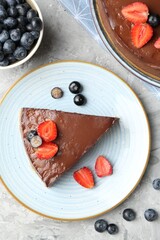 Piece of tasty chocolate cheesecake with berries on light grey textured table, flat lay