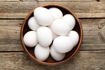 Fresh chicken eggs in bowl on wooden table, top view