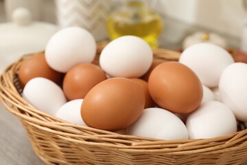 Raw chicken eggs in wicker basket on wooden counter indoors, closeup