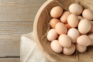 Raw chicken eggs and straw in bowl on wooden table, top view. Space for text