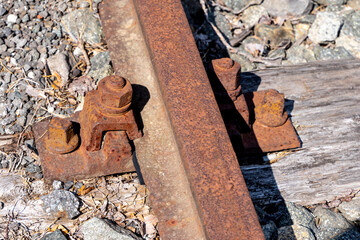 close up of rusty railway track with bolts and wooden sleeper in sunlight