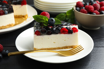 Piece of delicious cheesecake with berries and mint on black wooden table, closeup