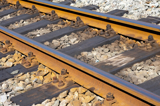 parallel railway tracks with wooden sleepers and gravel stones in sunlight