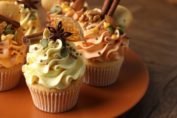 Delicious cupcakes with colorful cream, spices, cookies and nuts on wooden table, closeup