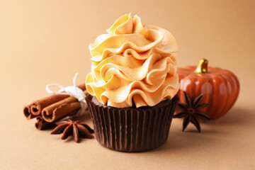 Delicious cupcake with colorful cream, anise stars, cinnamon and decorative pumpkin on beige background, closeup