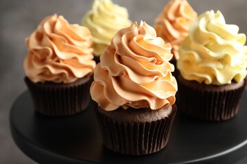 Delicious cupcakes with colorful cream against black stand on grey background, closeup