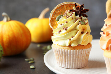 Delicious cupcakes with colorful cream, spices and autumn decor on grey table, closeup