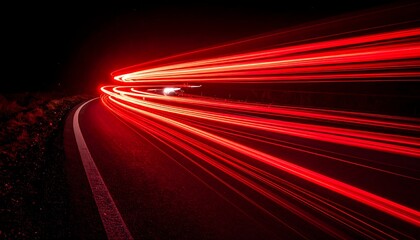A long exposure photograph captures red light trails from a moving vehicle traversing a dark, winding road at night, highlighting the motion