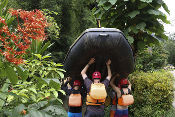 Outdoor adventure filled with teamwork. People are actively carrying large inflatable raft...