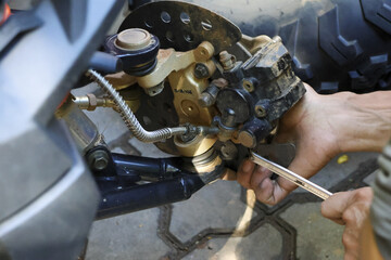 Mechanic with focused concentration performs motorcycle repair and maintenance. hand uses tool to fix vehicle front brake caliper in garage workshop