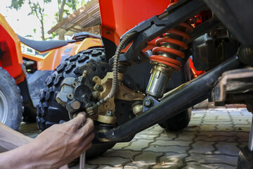 Focused mechanic hands doing vehicle repair on red quad bike. man fixes suspension and shock absorber with tool, concentrated on maintenance service outdoors © CoreRock