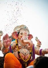 colorful ganesha idol decorated with vibrant garlands, surrounded by devotees with falling confetti, festive atmosphere. ganesh chaturthi celebration, hindu festival, cultural poster, greeting card