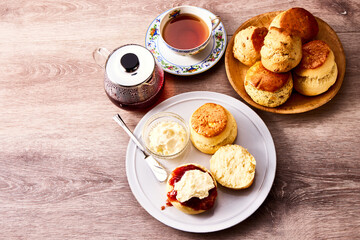 紅茶とともに楽しむアフタヌーンティーのスコーン。クロテッドクリームとジャムを添えて味わう伝統的な英国風ティータイムの一場面。ティーポットやカップと共に並べられたスコーンは、洋菓子、デザート、カフェ、休日のひとときを表現する素材写真として利用可能。