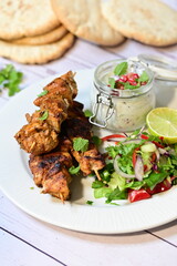 Chicken kebab served with raita and fresh salad on a white plate, light background, healthy and delicious popular meal.