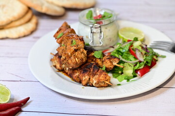 Chicken kebab served with raita and fresh salad on a white plate, light background, healthy and delicious popular meal.