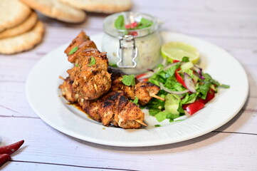 Chicken kebab served with raita and fresh salad on a white plate, light background, healthy and delicious popular meal.
