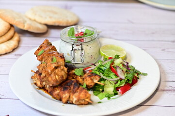 Chicken kebab served with raita and fresh salad on a white plate, light background, healthy and delicious popular meal.