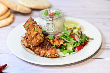 Chicken kebab served with raita and fresh salad on a white plate, light background, healthy and delicious popular meal.