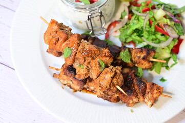Chicken kebab served with raita and fresh salad on a white plate, light background, healthy and delicious popular meal.