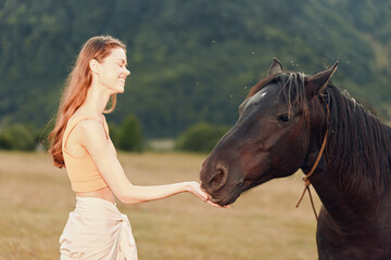 A cheerful woman in a peach top stands in a sunlit field, extending her hand to a calm horse. She smiles brightly as the horse nuzzles gently, creating a peaceful countryside moment.