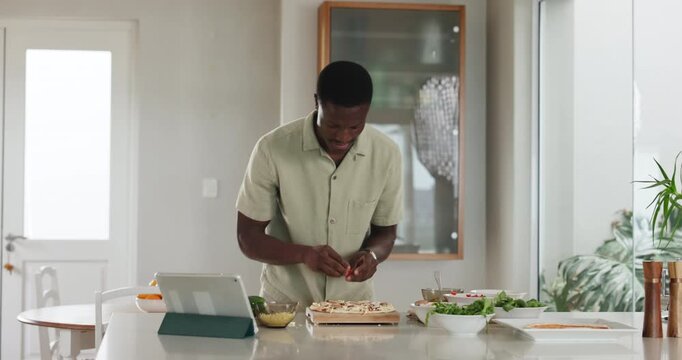 Man, cooking and pizza in kitchen with tablet, dance or online course with ingredients for meal. African person, food and tech with checklist, dough or virtual class on app for cuisine at apartment