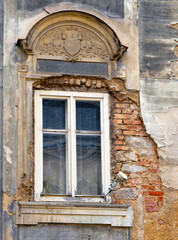 Old decayed window with decorative stone arch and crumbling brick wall and a modern satellite-antenna (directional antenna)